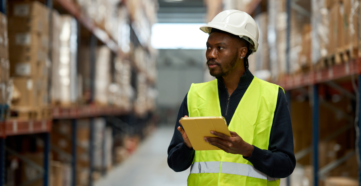 View of a modern warehouse with neatly organized racks and an operator using digital technology, illustrating the choice of the right WMS to improve logistics efficiency.
