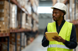 View of a modern warehouse with neatly organized racks and an operator using digital technology, illustrating the choice of the right WMS to improve logistics efficiency.